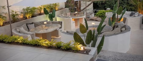An outdoor seating area with a round table and chairs, surrounded by planters and under umbrellas.