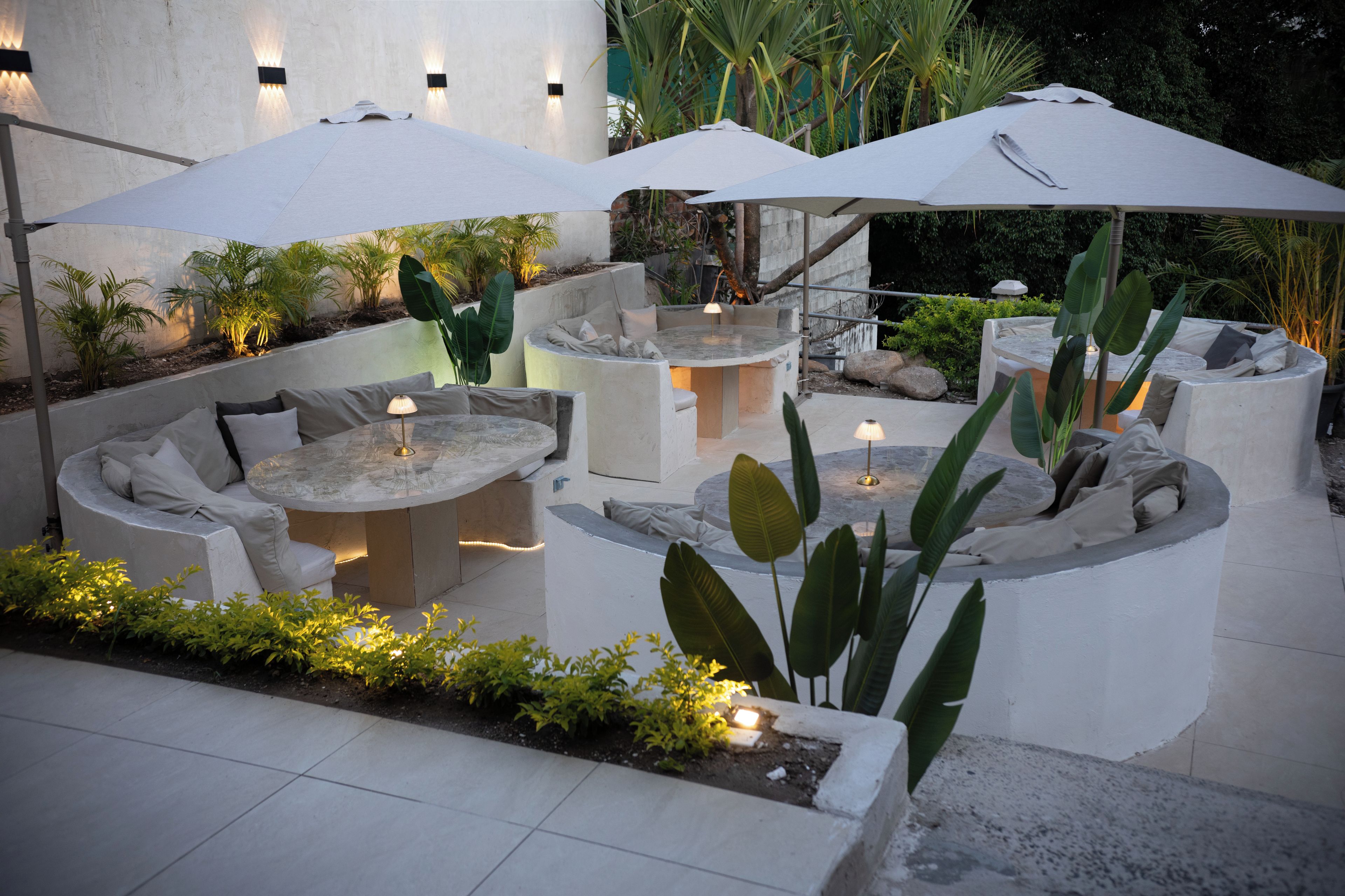 An outdoor patio area with a round table and seating, surrounded by planters and umbrellas.