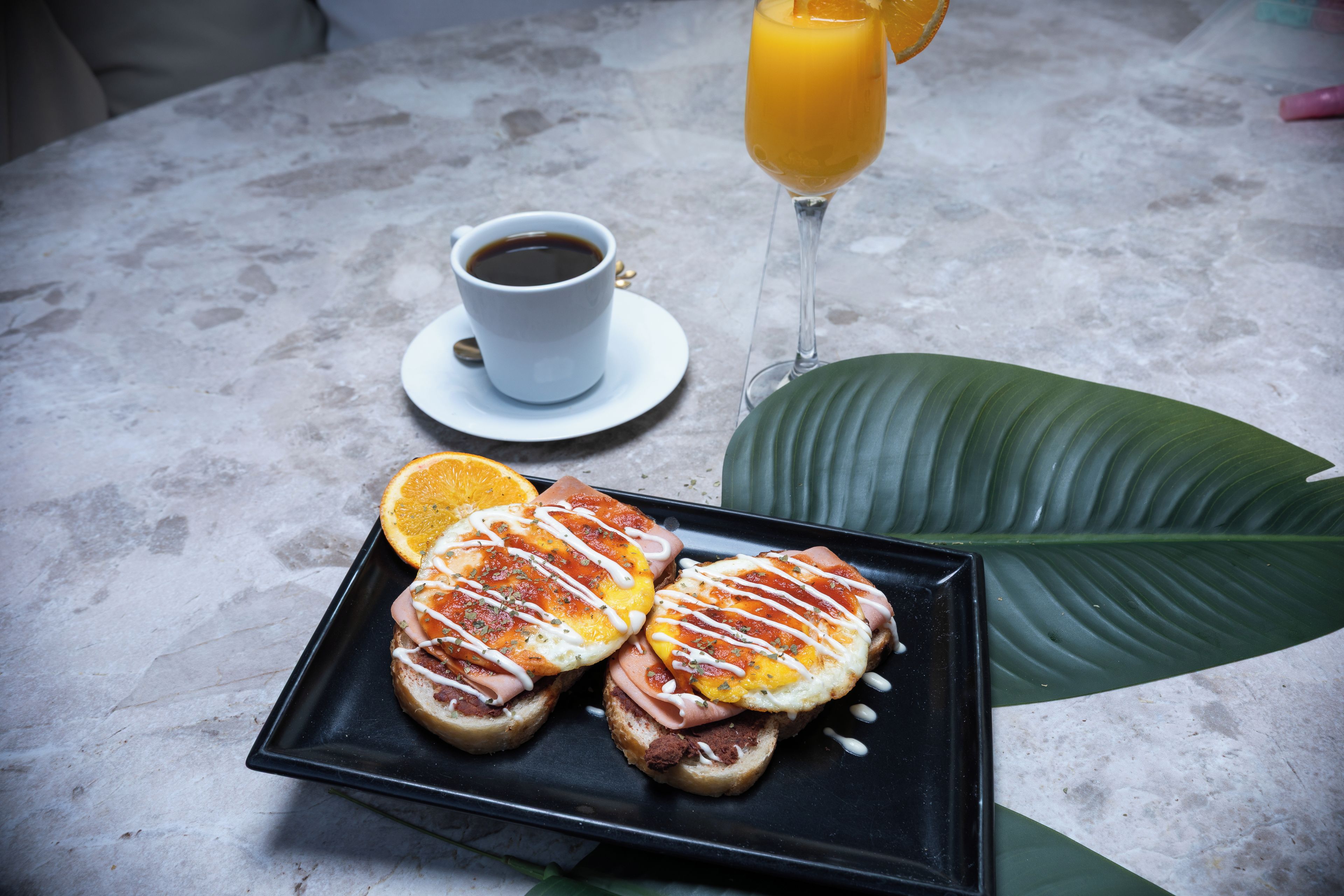 Une table en marbre dressée pour le petit-déjeuner, avec une assiette de sandwichs, une tasse de café et un verre de jus d’orange.