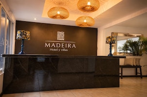 Balcão de recepção de hotel com bancada de mármore escura, um logotipo e duas lâmpadas decorativas.