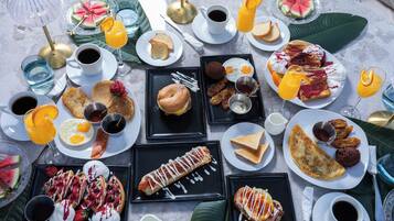 A variety of breakfast items including pancakes, eggs, waffles, and pastries, arranged on multiple plates and trays.