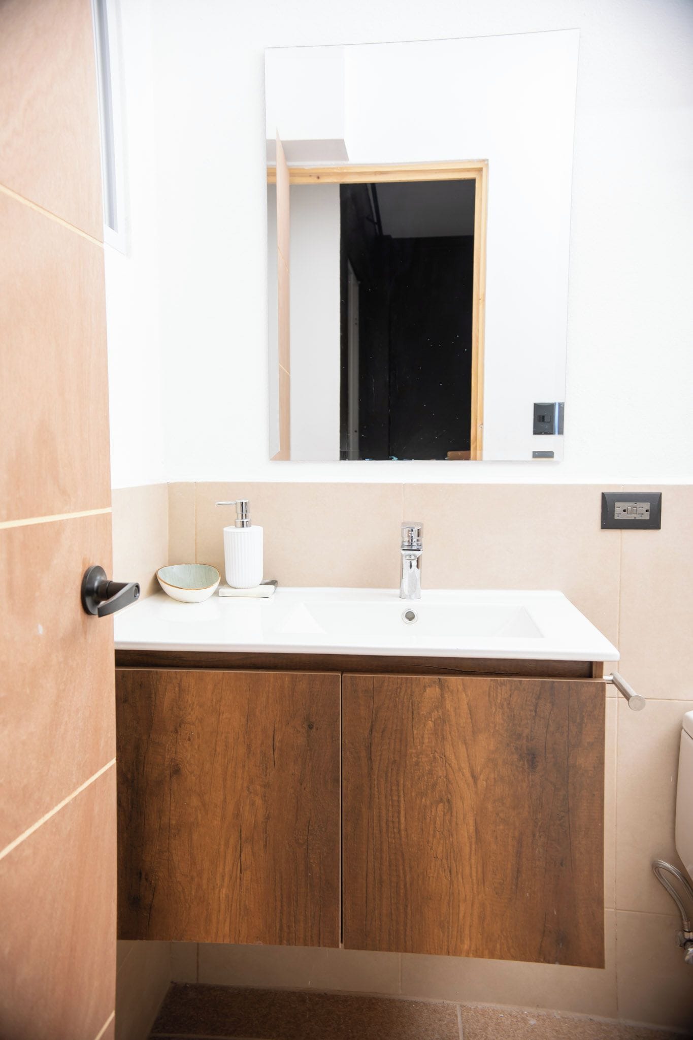 Un baño con tocador de madera, un lavamanos blanco, un espejo y un inodoro.