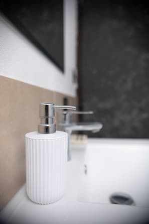 A bathroom with a white sink, a chrome faucet, and a white soap dispenser.