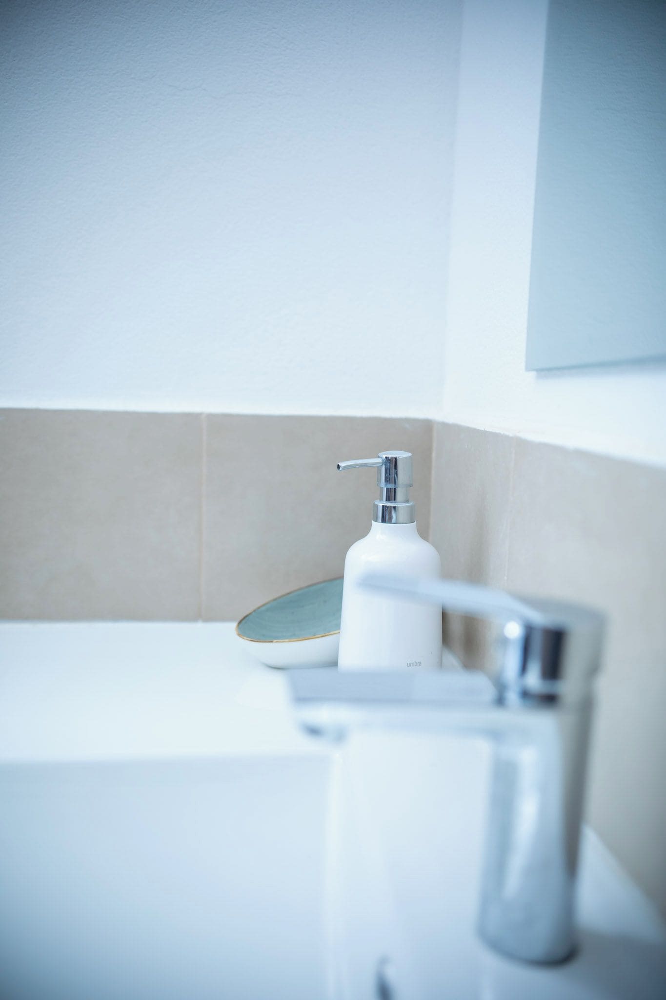 A bathroom with a white sink, a chrome faucet, and a soap dispenser.
