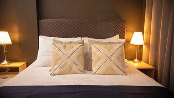 A hotel room with a large bed, two bedside lamps, and a headboard with a diamond pattern.