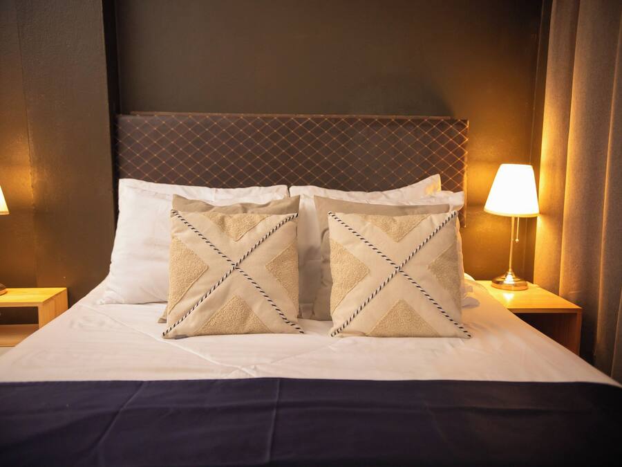 A hotel room with a large bed, two bedside lamps, and a headboard with a diamond pattern.