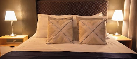 A neatly made bed with two pillows, a dark bedspread, and two bedside lamps on wooden nightstands.