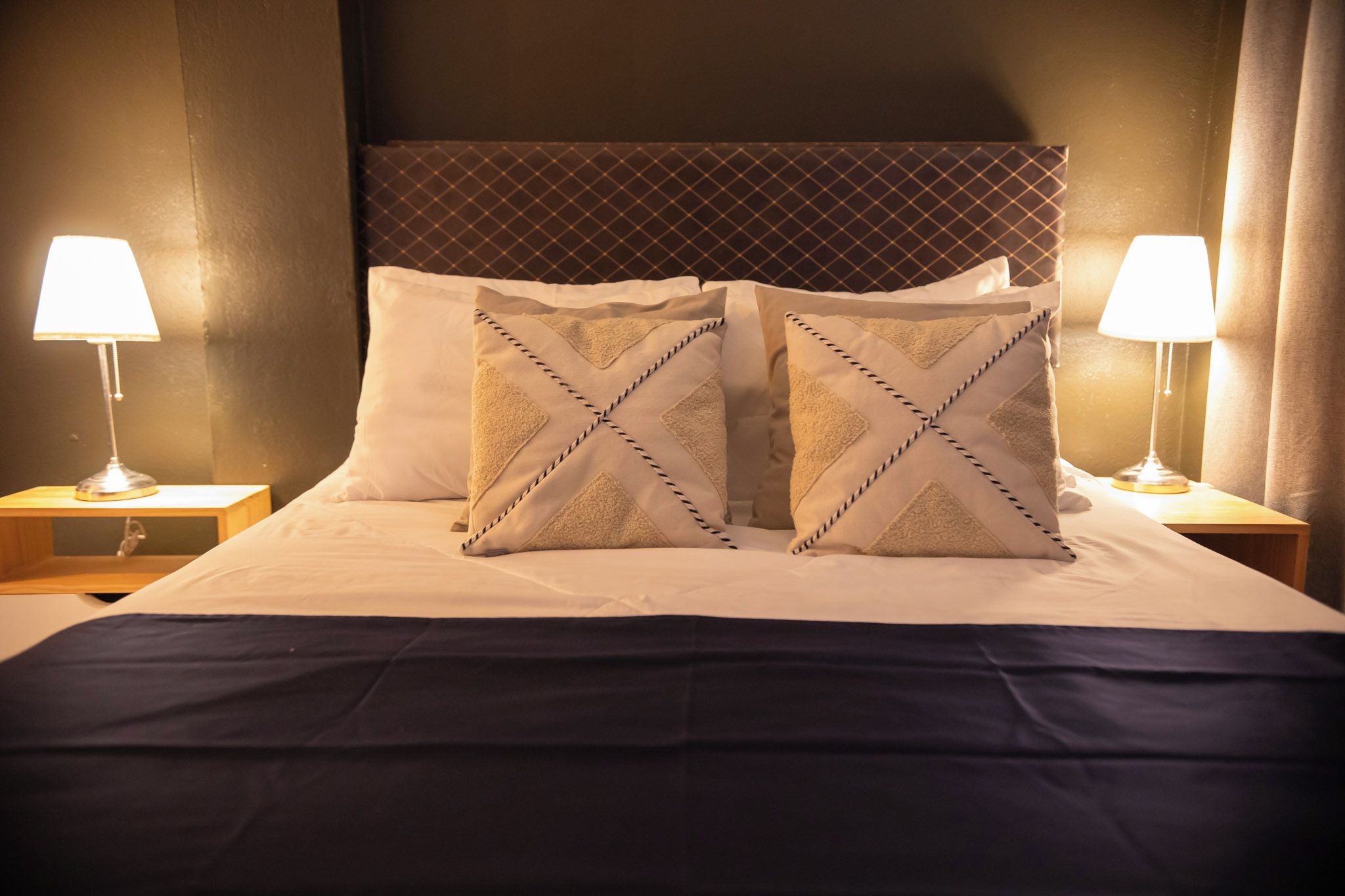 Een hotelkamer met een bed, twee nachtkastjes, twee lampen en twee decoratieve kussens.