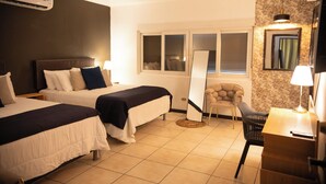 Ein Hotelzimmer mit zwei Betten, einem Schreibtisch, einem Stuhl, einem Spiegel und einem Fenster mit Jalousien.