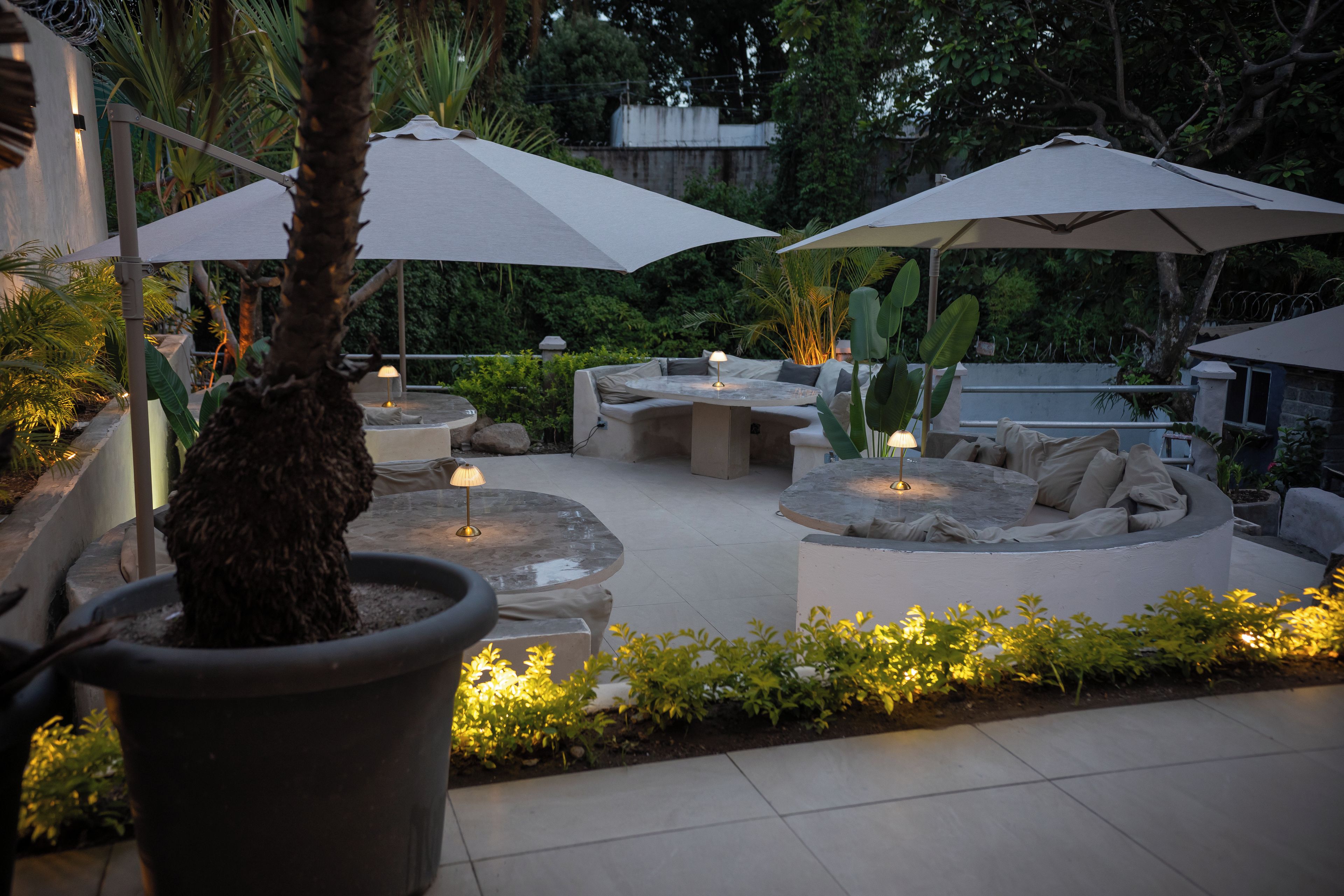 An outdoor patio area with seating arrangements, including a round table and a sofa, under large umbrellas.
