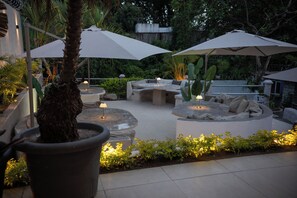 An outdoor patio area with seating arrangements, including a round table and a sofa, under large umbrellas.