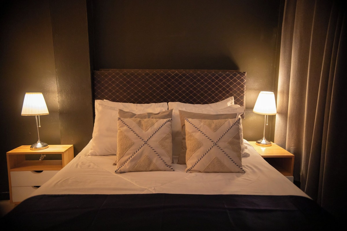 A hotel room with a bed, two bedside lamps, and a headboard.
