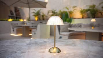 Una mesa con una lámpara moderna en un área exterior bien iluminada, con sombrillas y plantas.
