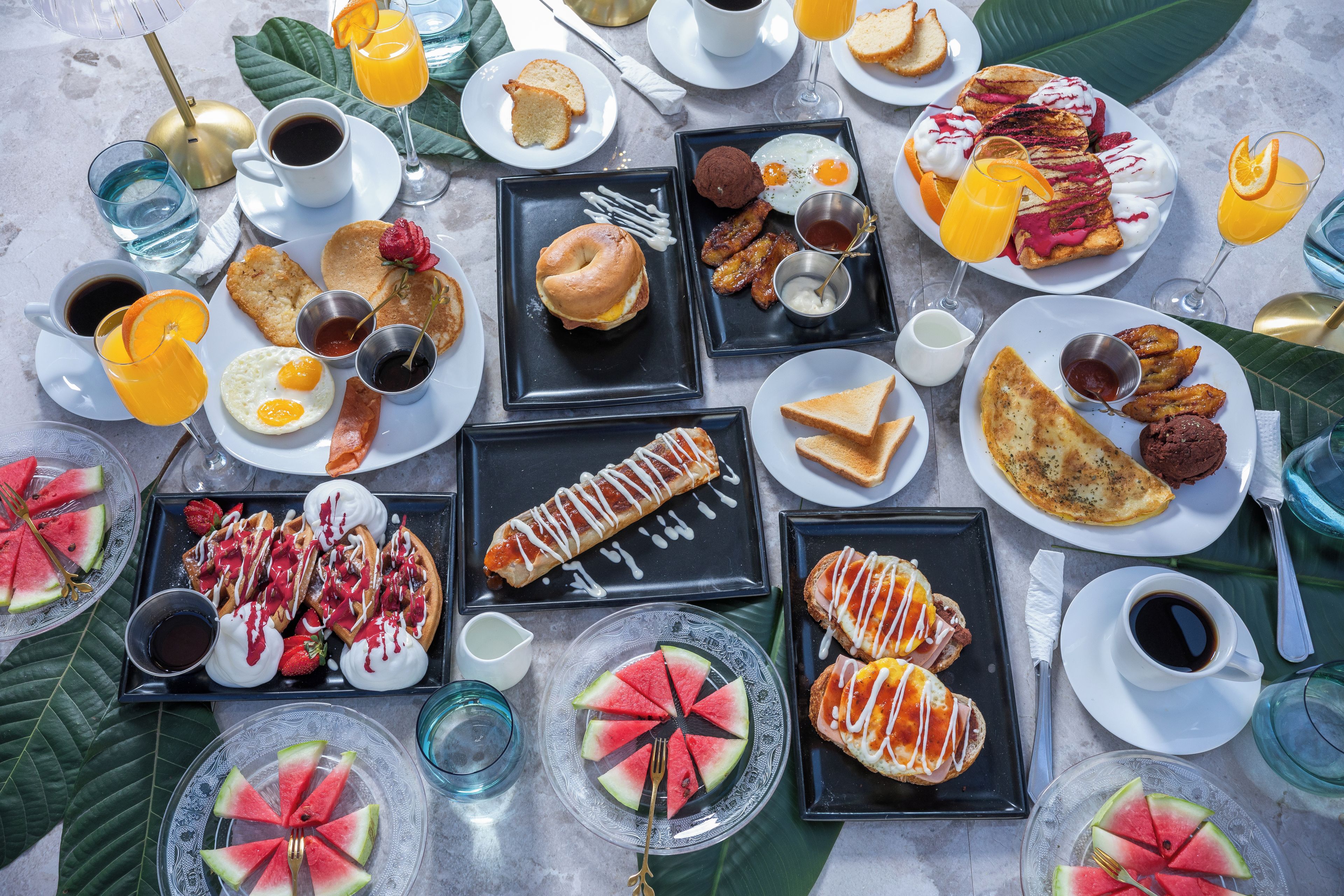 A variety of breakfast items including waffles, pancakes, eggs, and pastries, arranged on a table with multiple plates and cups.