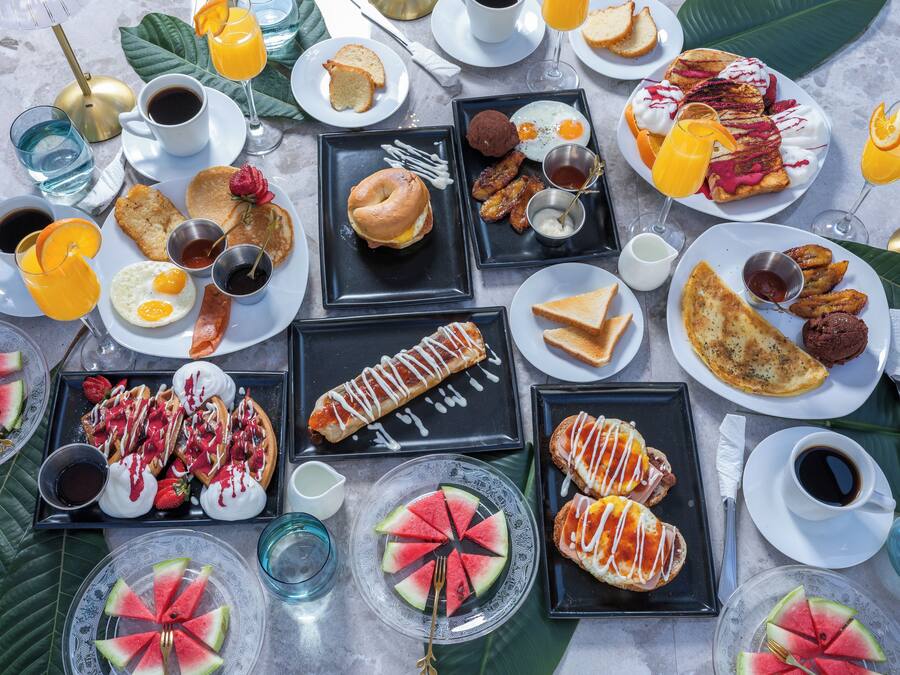 A variety of breakfast items including waffles, pancakes, eggs, and pastries, arranged on a table with multiple plates and cups.