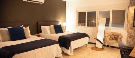 A hotel room with two beds, a chair, a desk, and a large window.