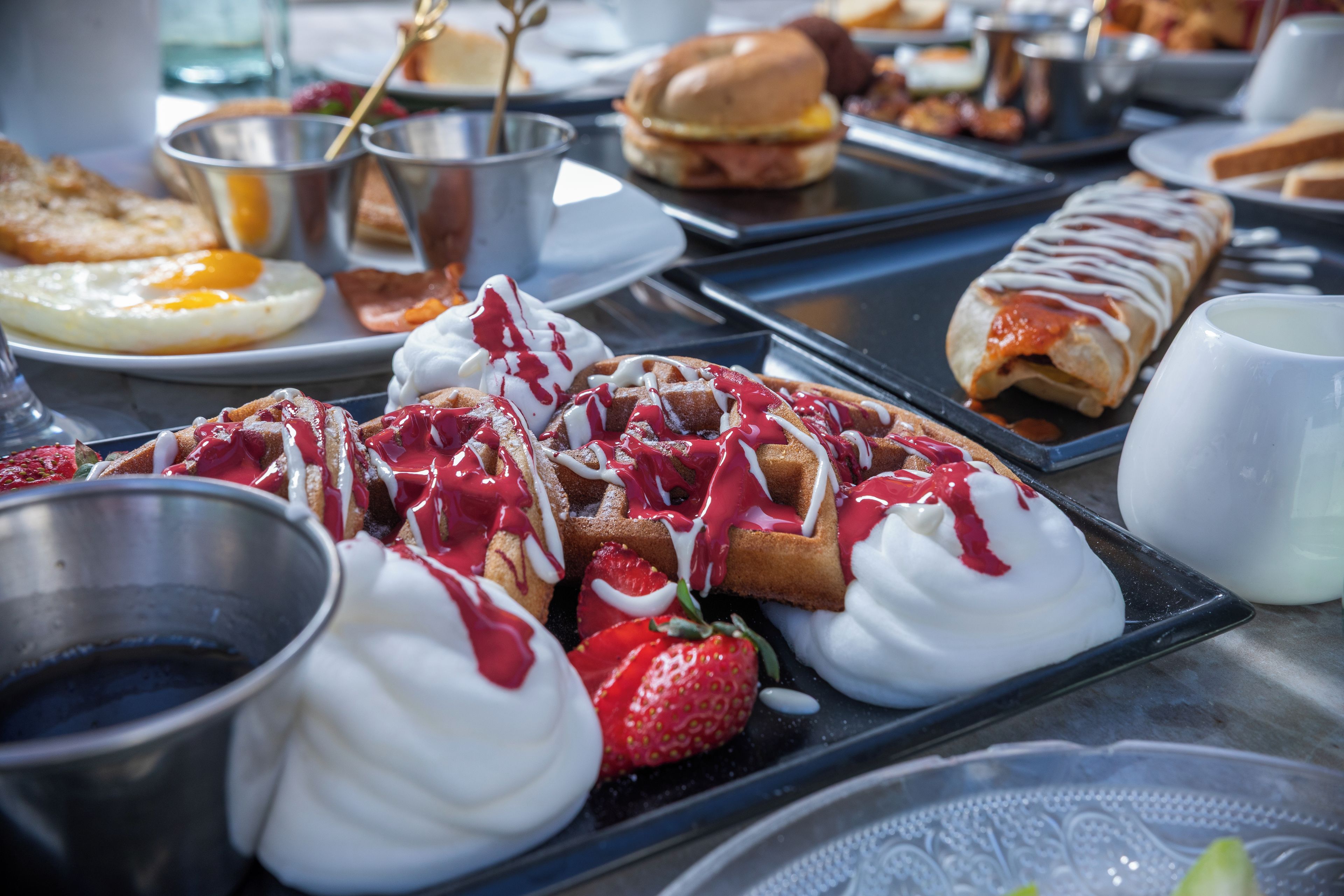 A variety of breakfast items including waffles, pancakes, and pastries on a tray.