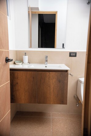Une salle de bain avec un meuble-lavabo en bois, un lavabo blanc, un miroir et des toilettes.