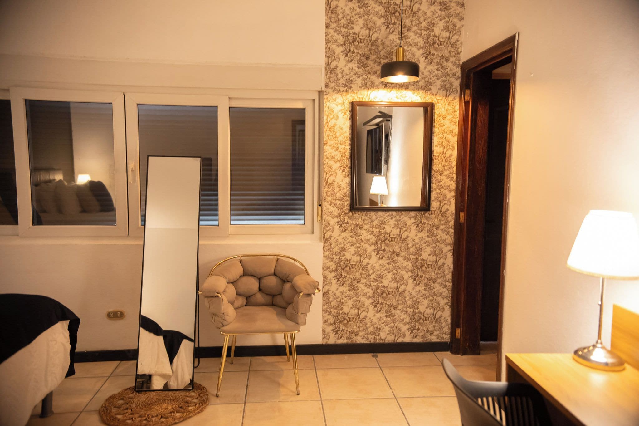 A room with a bed, a chair, a mirror, and a lamp.
