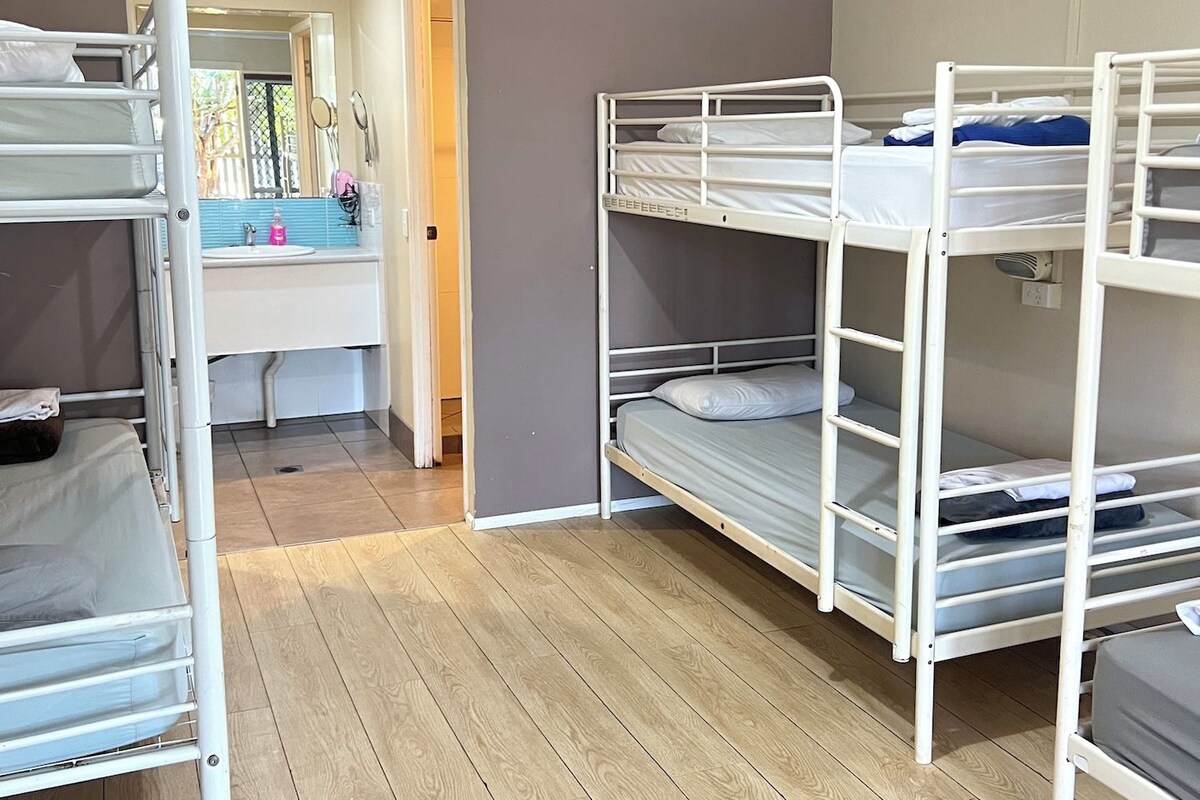 A room with bunk beds, a bathroom with a sink, and a door leading to another room.