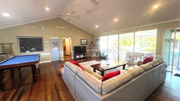 A living room with a pool table, a sofa, a television, and a balcony with outdoor seating.