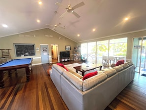 A living room with a pool table, a sofa, a television, and a balcony with outdoor seating.