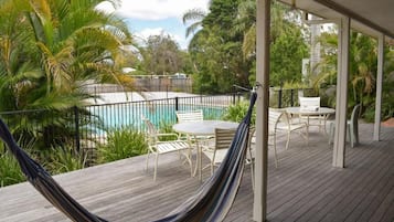 Un patio in legno con un'amaca, mobili da esterno e vista su una piscina.