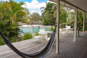 A wooden deck with a hammock, outdoor furniture, and a view of a swimming pool. - Flashpackers Hervey Bay (Torquay)