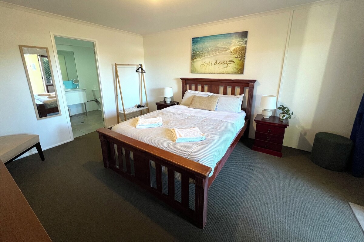 A bedroom with a wooden bed, a bedside table with a lamp, a mirror, and a painting on the wall.