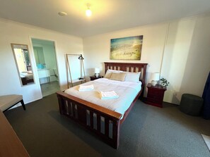 A bedroom with a wooden bed, a bedside table with a lamp, a mirror, and a painting on the wall. - Flashpackers Hervey Bay (Torquay)