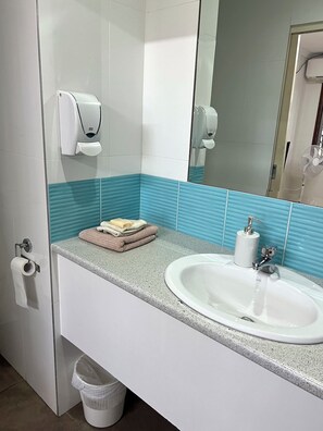 A bathroom with a white sink, a mirror, a towel rack, and a hand dryer. - Flashpackers Hervey Bay (Torquay)
