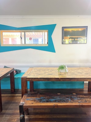 A room with a wooden table, a bench, and a wall with a blue design and a framed picture. - Flashpackers Hervey Bay (Torquay)