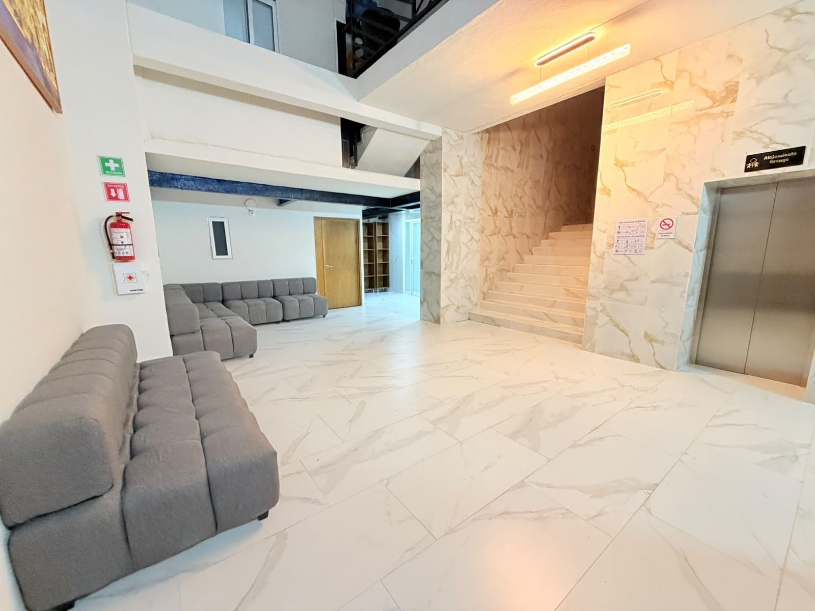 A spacious lobby with a grey sectional sofa, a marble floor, and a staircase leading to an upper level.