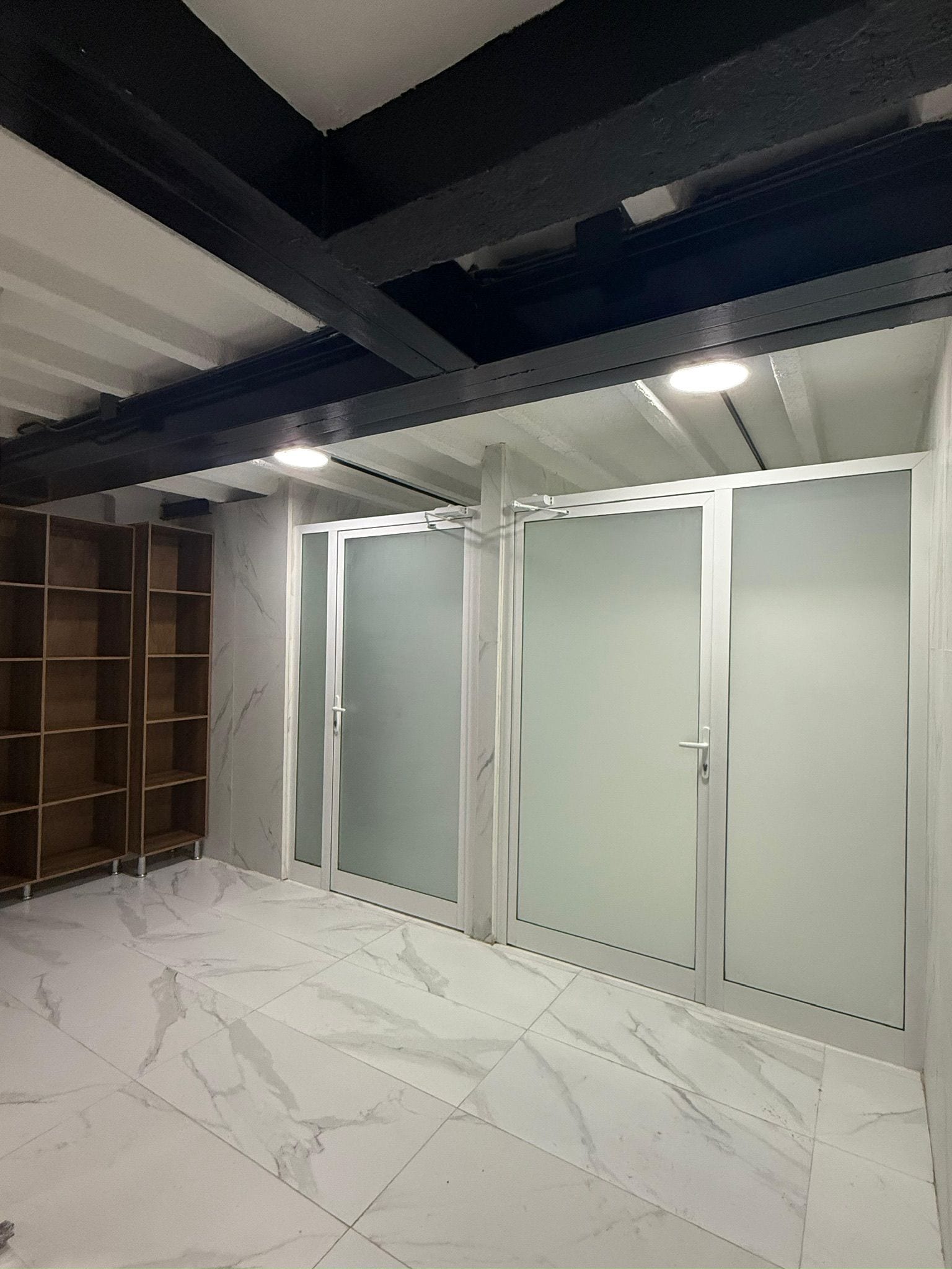 A room with a marble floor, a wooden shelving unit, and a set of frosted glass doors.