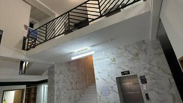 A spacious interior with a marble staircase, a second-floor balcony with a metal railing, and an elevator.