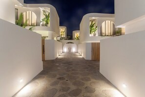 A nighttime view of a modern building with a central courtyard, illuminated by ground lights, and surrounded by white walls with large windows. - Kona Resort Pererenan F (Badung)