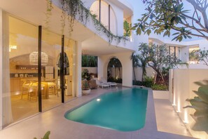 A modern outdoor pool area with a glass-enclosed dining space and a kitchen visible through the glass. - Kona Resort Pererenan F (Badung)