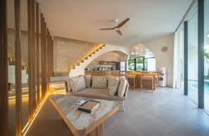 A modern living room with a sofa, coffee table, and a staircase with wooden railings. - Kona Resort Pererenan F (Badung)