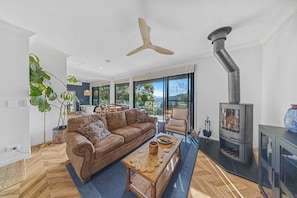 A modern living room with a brown leather sofa, a wooden coffee table, and a large window. - Fletchers Ridge Guest House (Montville)