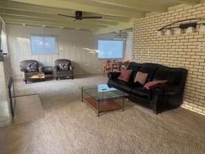 A living room with a black leather sofa, two striped armchairs, a glass coffee table, and a brick accent wall. -     Cozy 3BR Monterey Retreat – Close to Beach & Attractions (Monterey)