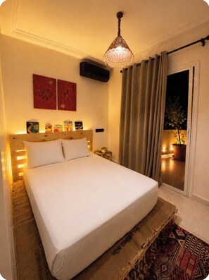 Een hotelkamer met een groot bed, een nachtkastje, een wandairco en een raam met gordijnen.