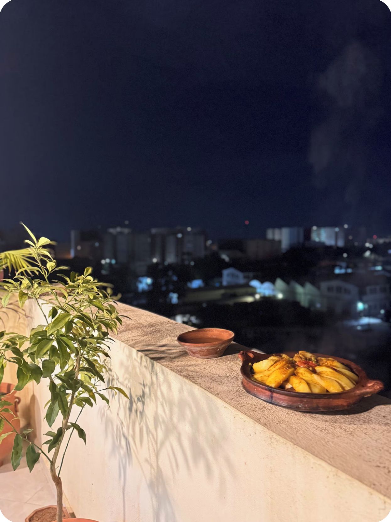 A balcony with a potted plant, a clay pot, and a dish of bananas.