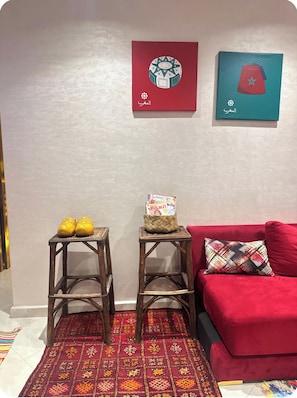 Een kamer met een rode bank, twee houten krukken, een kamerkleed met een patroon en twee objecten aan de muur bevestigd.