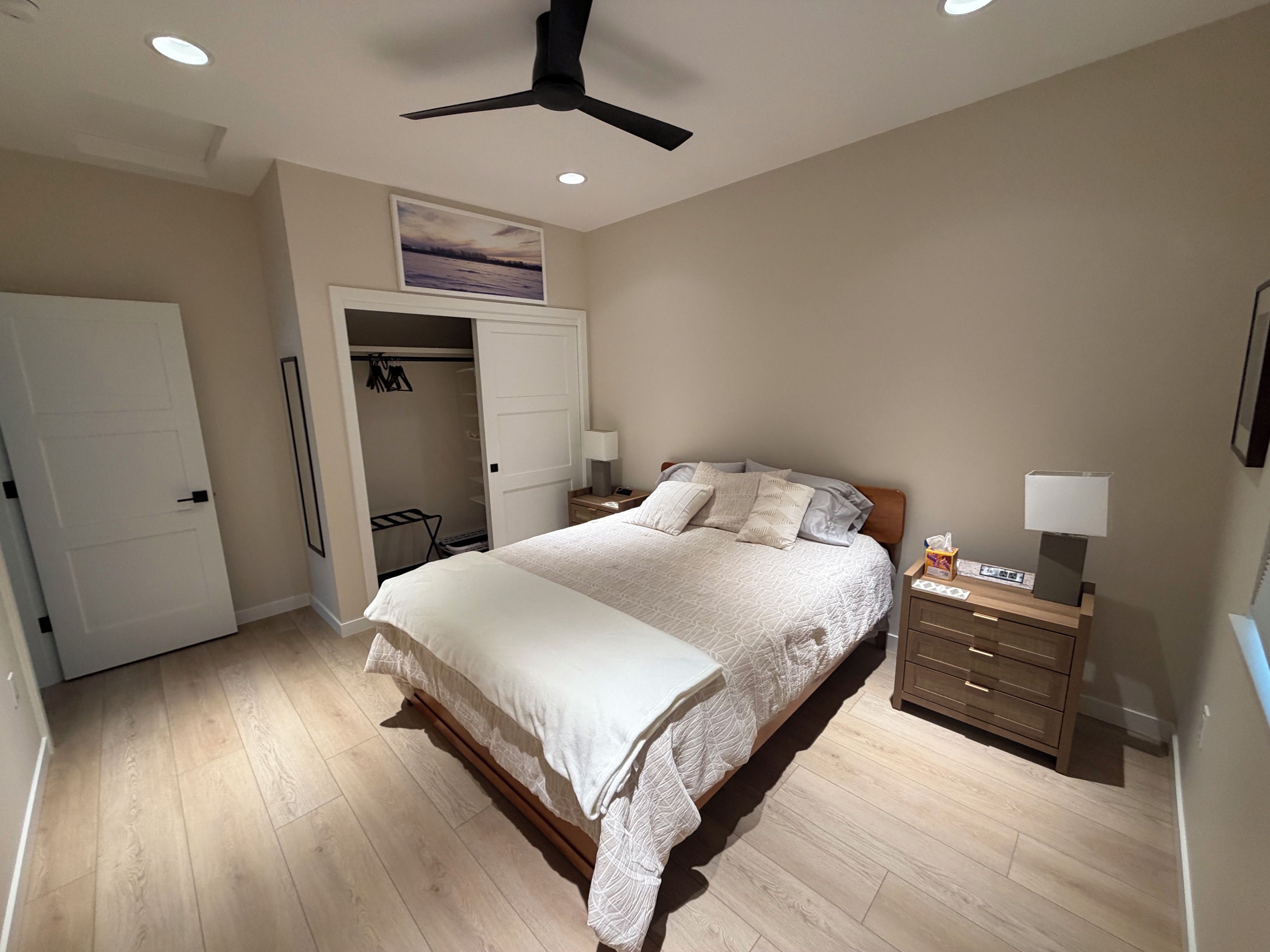 A bedroom with a bed, bedside table, nightstand, and a ceiling fan.