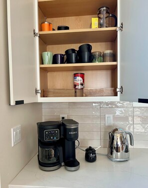 A kitchen with a coffee maker, a sugar container, and a kettle on the counter. - Ravens Rest - a Modern Stay in Midtown Anchorage. (Anchorage)