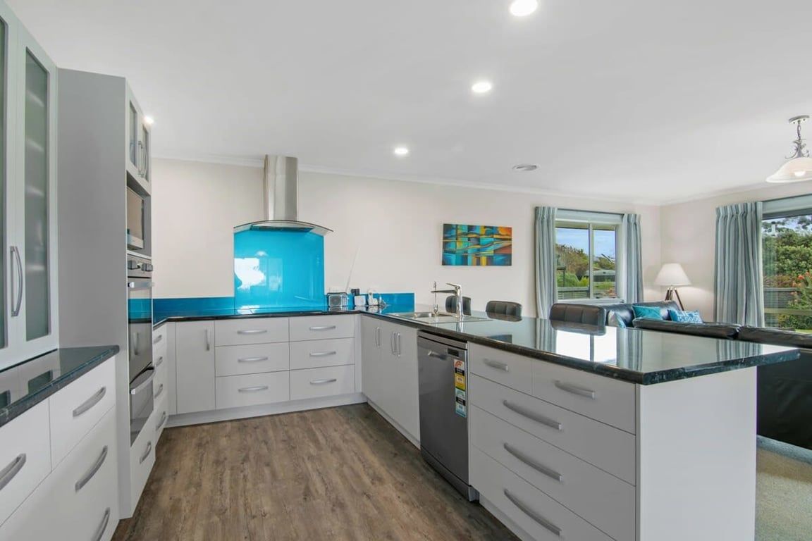 A modern kitchen with white cabinets, a blue backsplash, and a built-in dishwasher.
