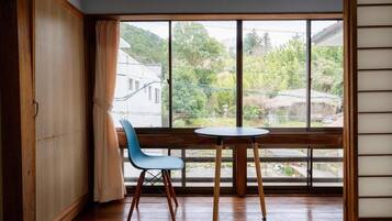 Une pièce avec un plancher en bois, une chaise bleue, une petite table ronde et une vue sur un quartier résidentiel, visible à travers de grandes fenêtres.