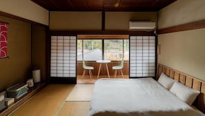 A traditional Japanese room with tatami flooring, a bed with white bedding, a sliding door with a view, and a small table with chairs. - Tawarayama Machigoto Ryokan (Nagato)
