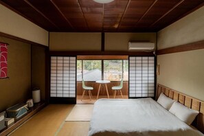 A traditional Japanese room with tatami flooring, a bed with white bedding, a sliding door with a view, and a small table with chairs. - Tawarayama Machigoto Ryokan (Nagato)