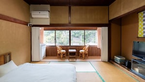 A room with a bed, a television, a window with curtains, and a view of greenery outside. - Tawarayama Machigoto Ryokan (Nagato)